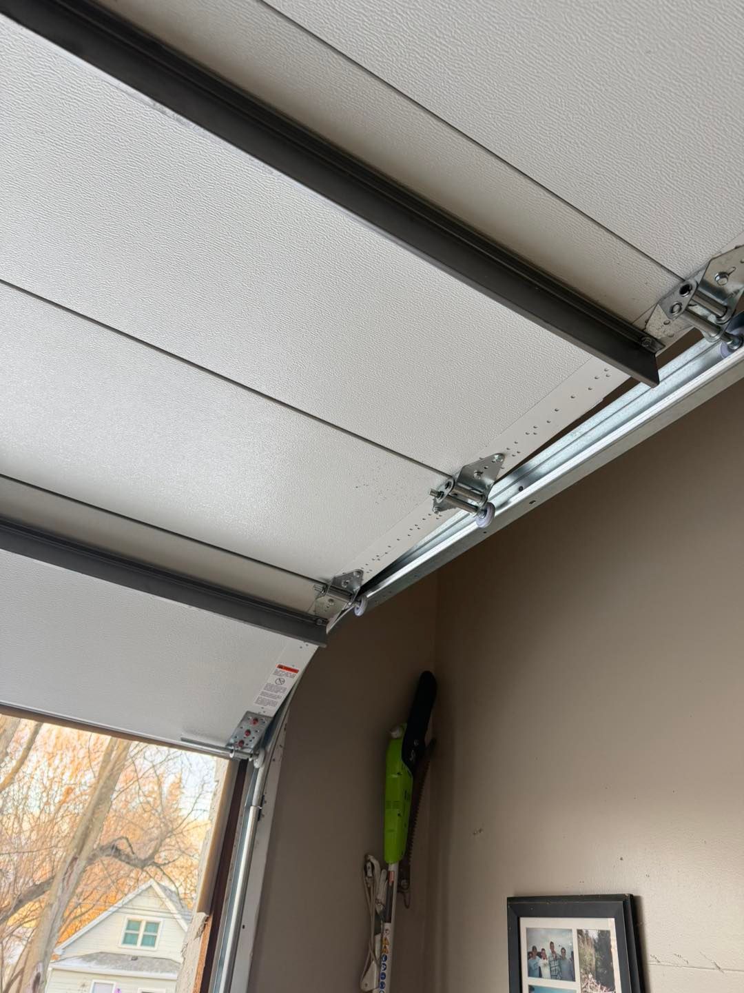 Garage door mechanism showing tracks, hinges, cables, and panels.