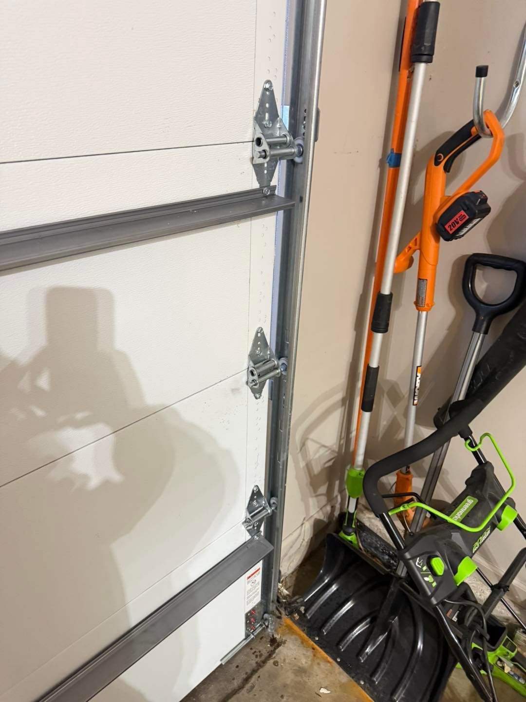 Garage door section with hinges, tools leaning against the wall.