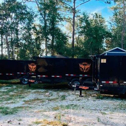 A black trailer with a deer logo on it is parked in a field.