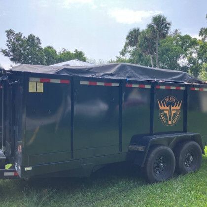 A black dump trailer is parked in a grassy field.