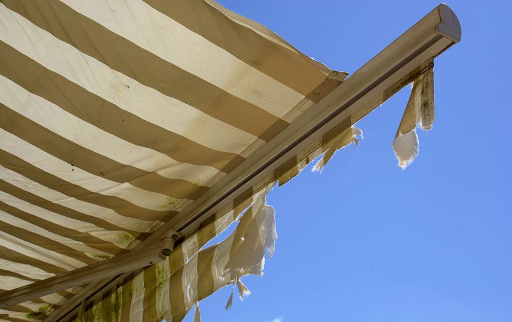 Zerrissene, gestreifte beige-weiße Markise vor strahlend blauem Himmel.
