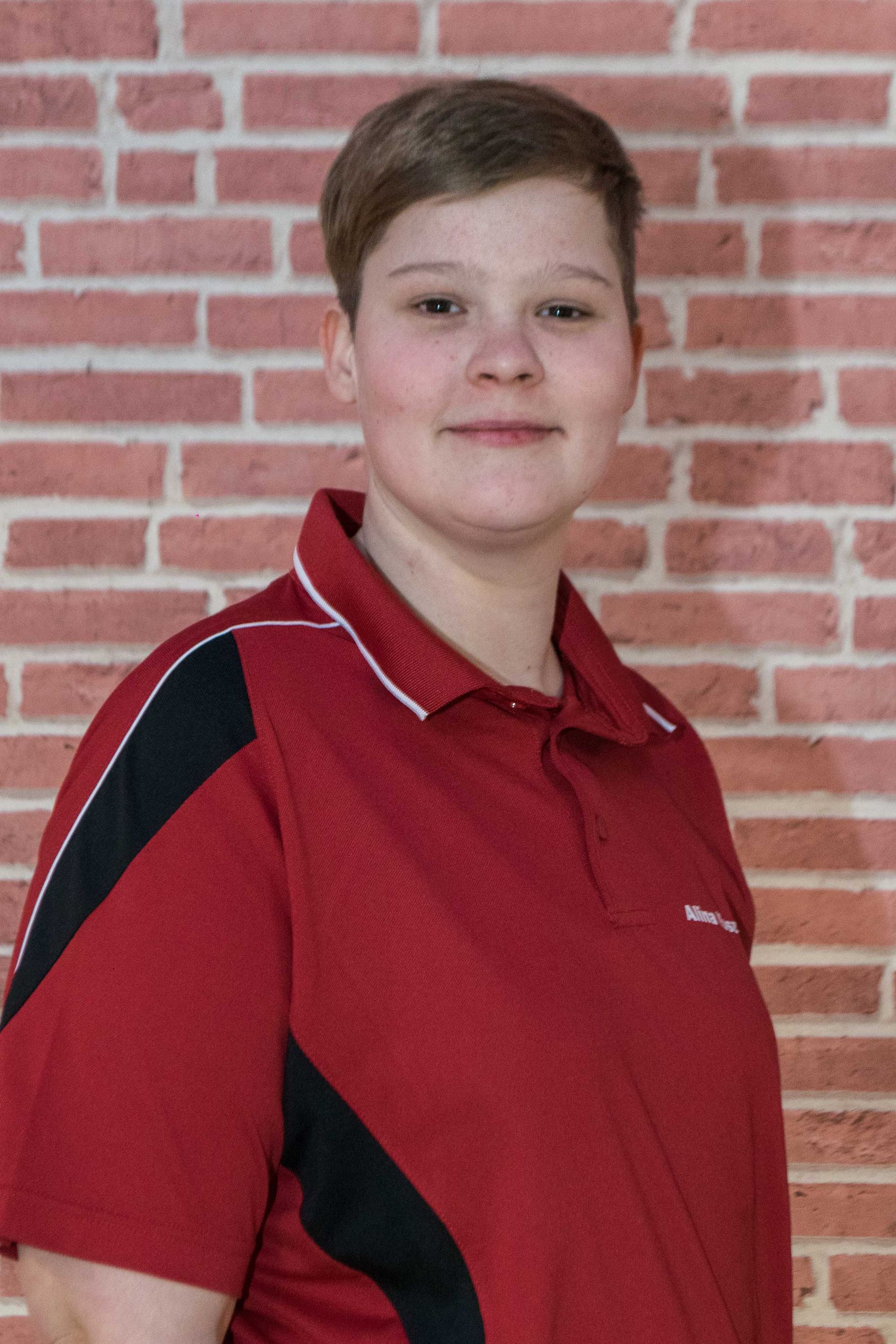 Alina Koszla in einem roten Hemd steht vor einer Backsteinmauer.