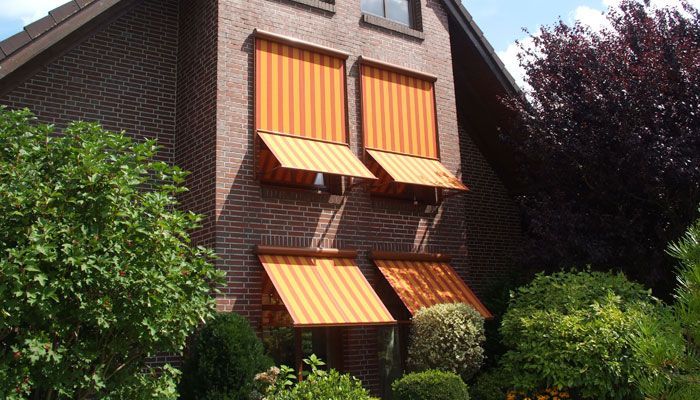 Ein Backsteinhaus mit orange gestreiften Markisen an den Fenstern. Fensterbeschattung von Terrassenwelten Frank Merz