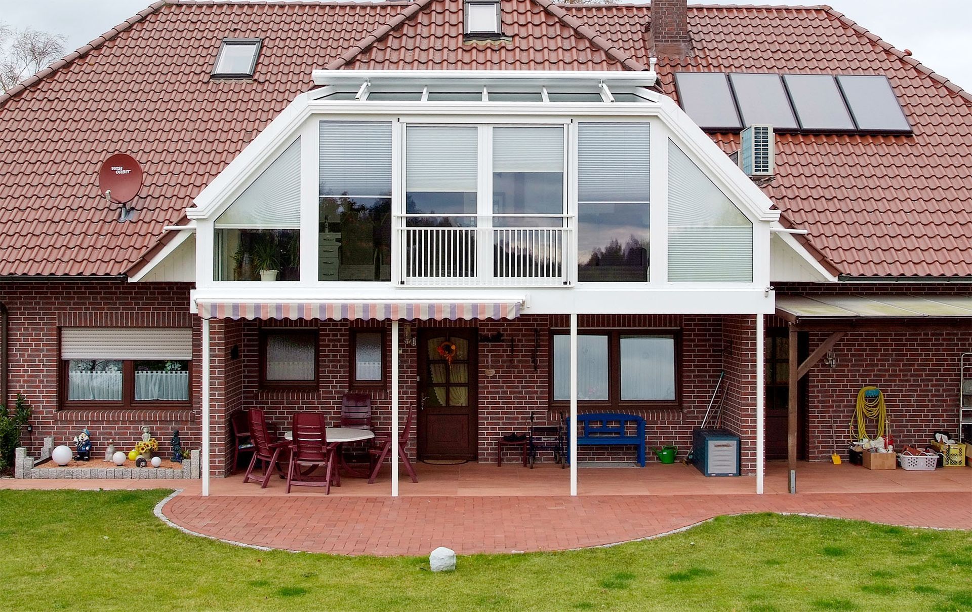 Ein großes Backsteinhaus mit einer weißen Veranda und einem roten Dach. Nachherbild