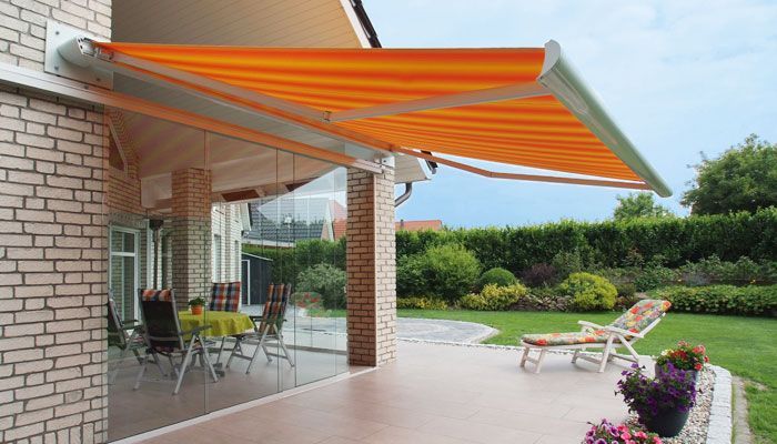 Eine Terrasse mit Tisch und Stühlen unter einer orangefarbenen Markise. Markisen von Terrassenwelten Frank Merz