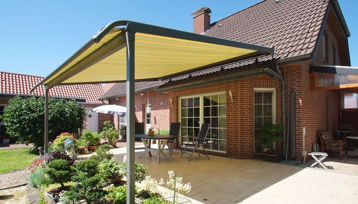 Eine Terrasse mit Überdachung und einem Tisch und Stühlen vor einem Backsteinhaus.