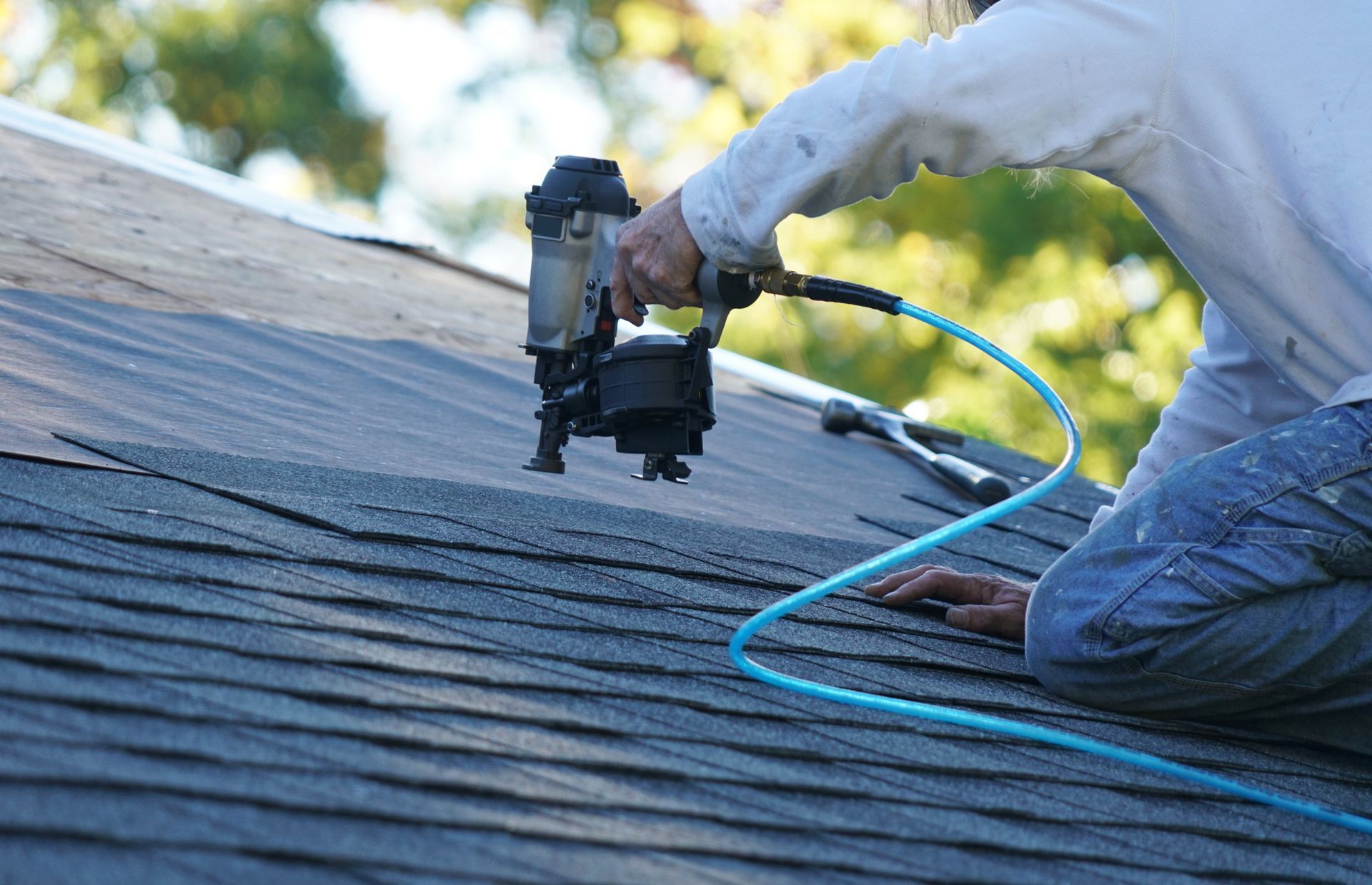 A man diligently uses a nail gun to repair a roof, securing shingles in place with focused precision.