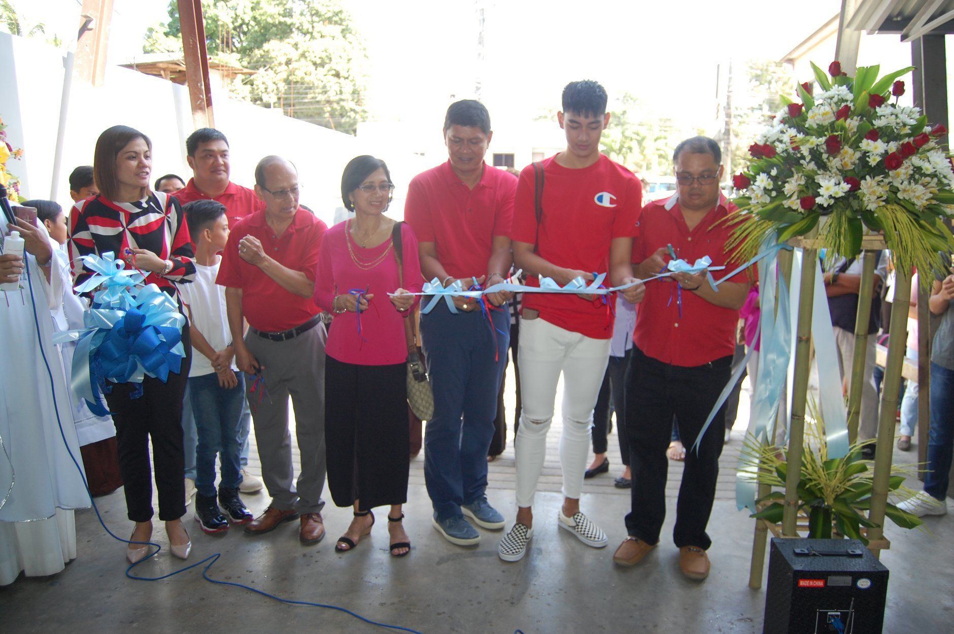 A group of people in red shirts are cutting a ribbon