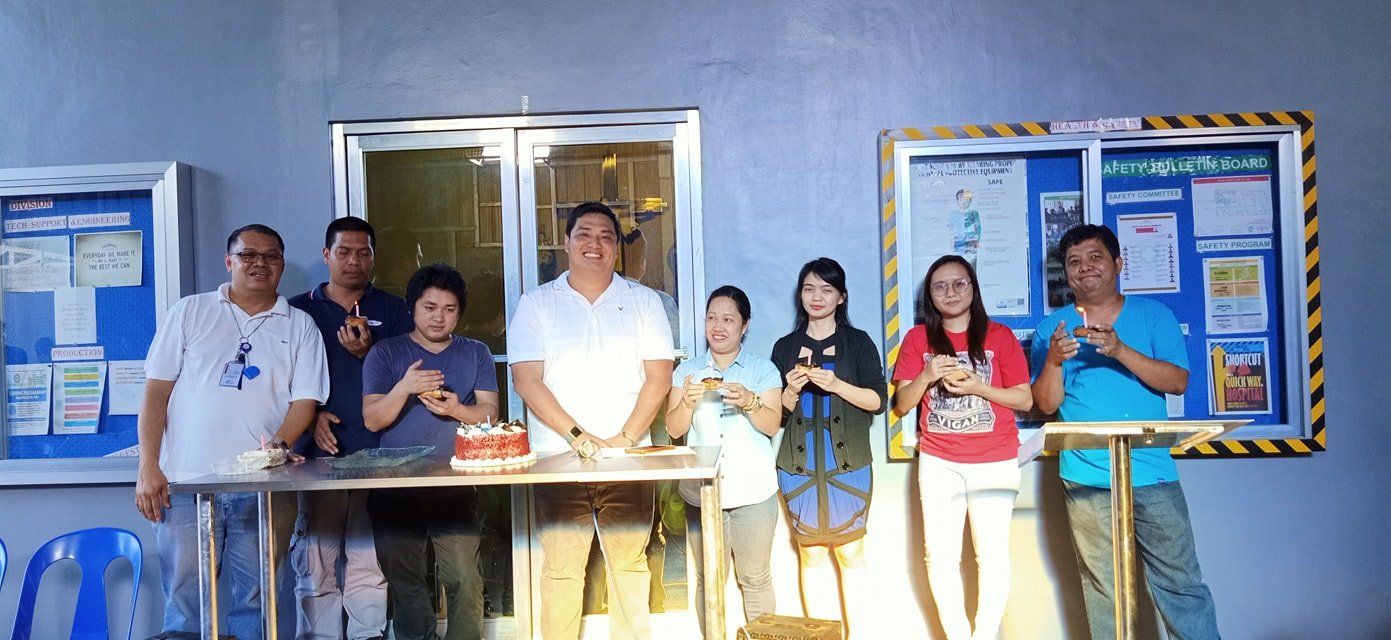A group of people are standing around a table with a cake on it.
