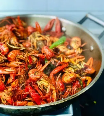 A pan filled with shrimp and vegetables is cooking on a stove.