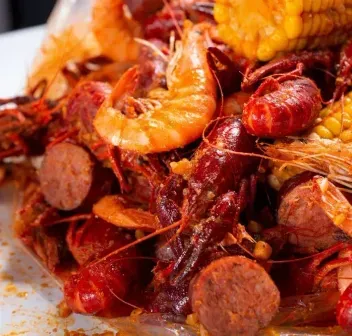 A close up of a plate of food with shrimp and corn on the cob.