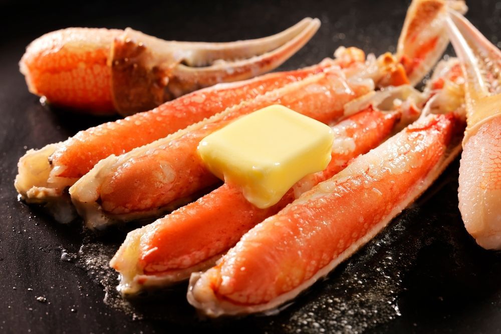 Crab legs with butter on top of them on a black plate.