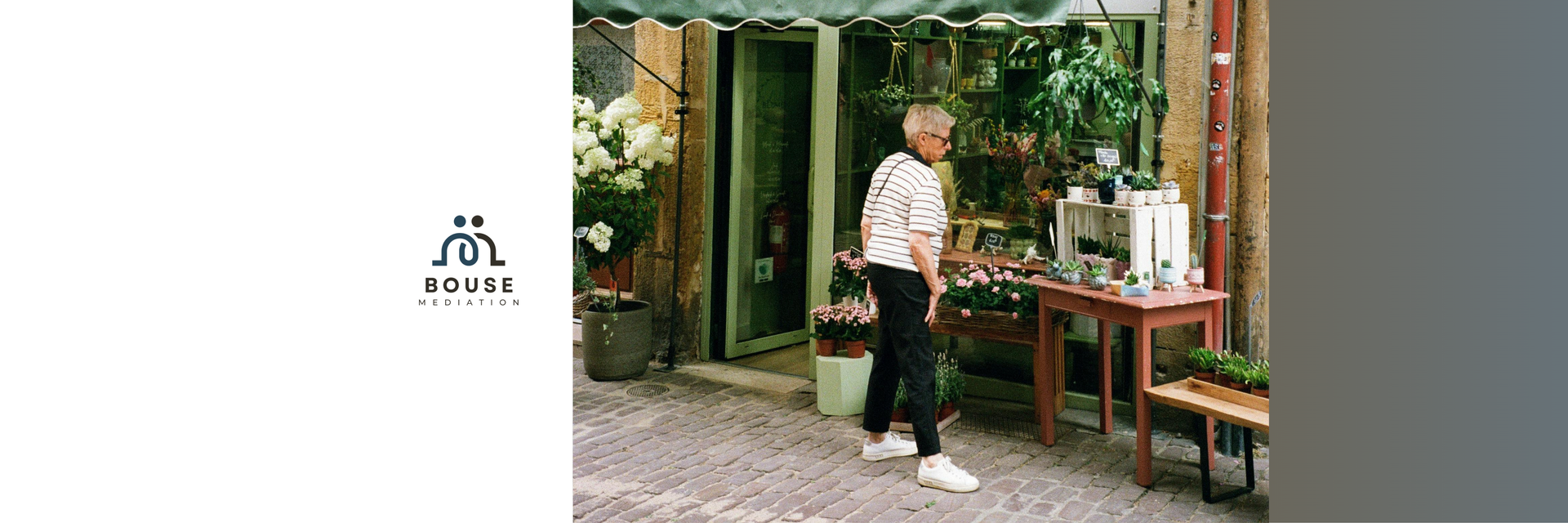 A person stands by a small table displaying goods in front of a greenery-filled shop entrance.