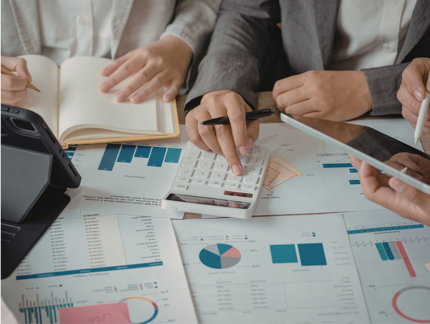 Colleagues reviewing financial charts and using a calculator on a desk filled with business documents.