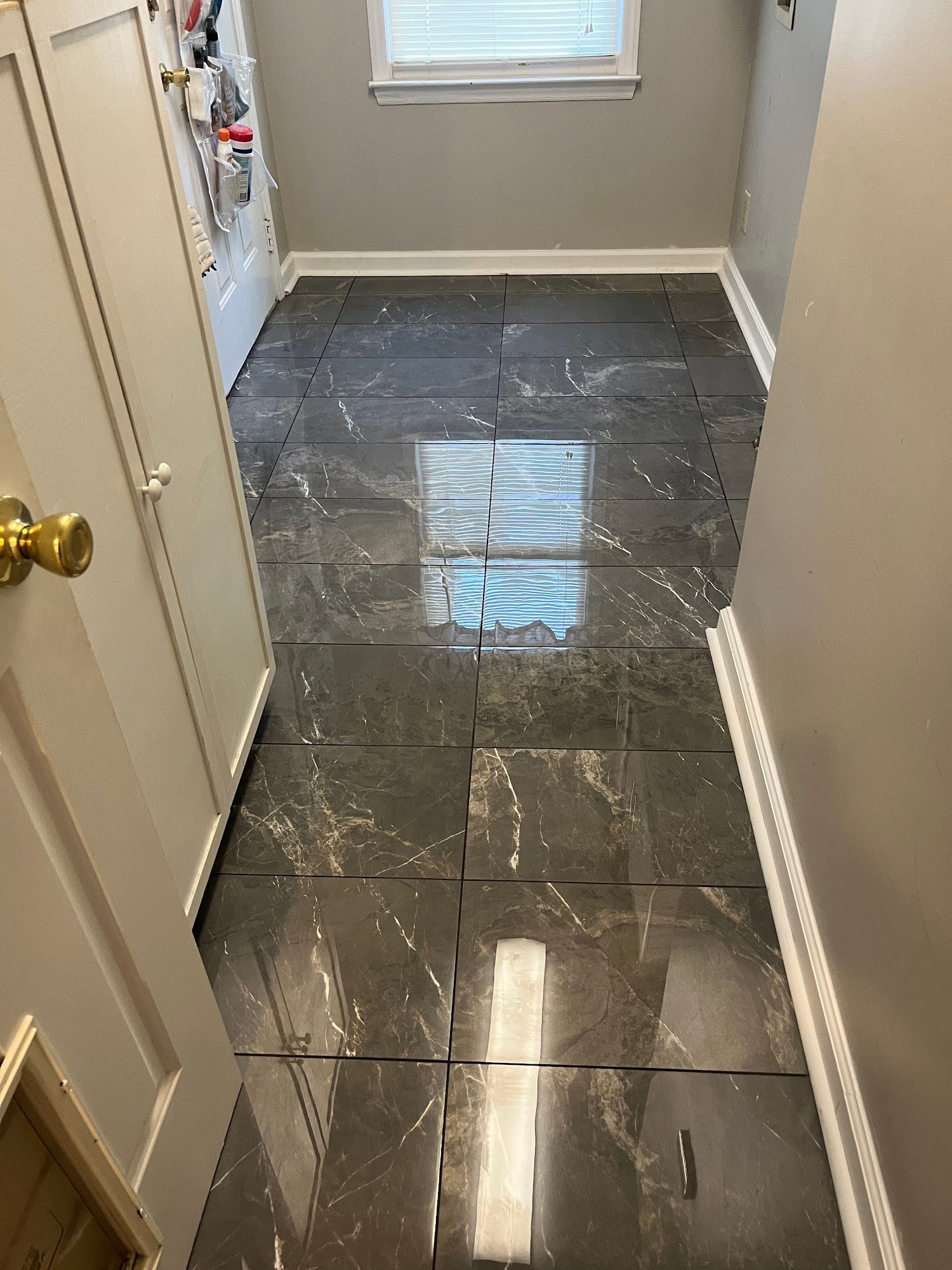 Dark gray marble-look tile flooring in a narrow hallway with a door, window, and white trim.