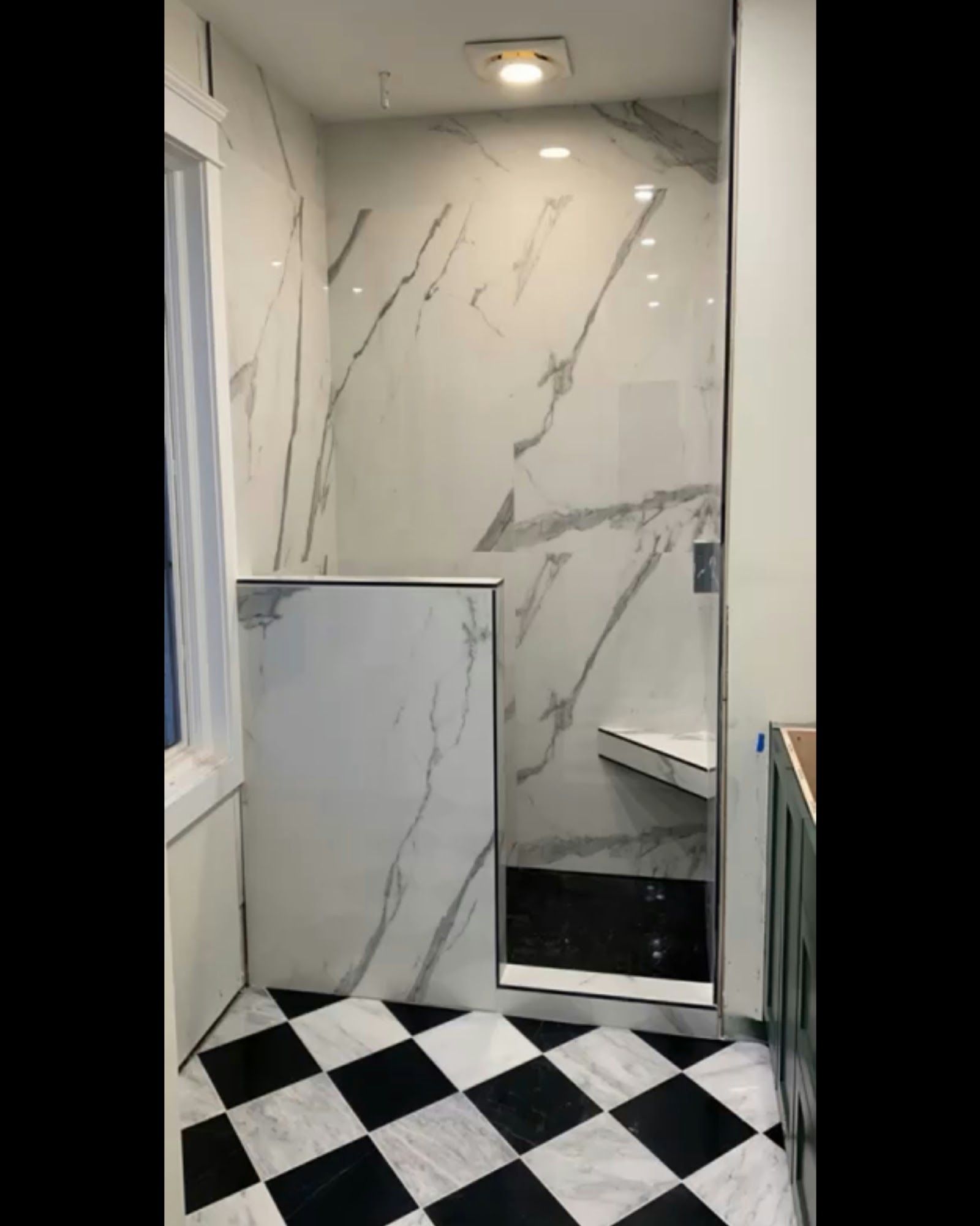 Modern shower with marble walls, glass door, checkerboard floor. Includes a built-in bench.