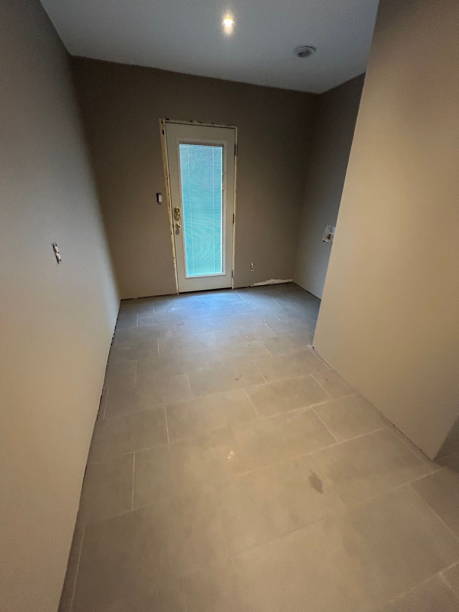A small room with gray tile flooring, a door with a window, and beige walls.