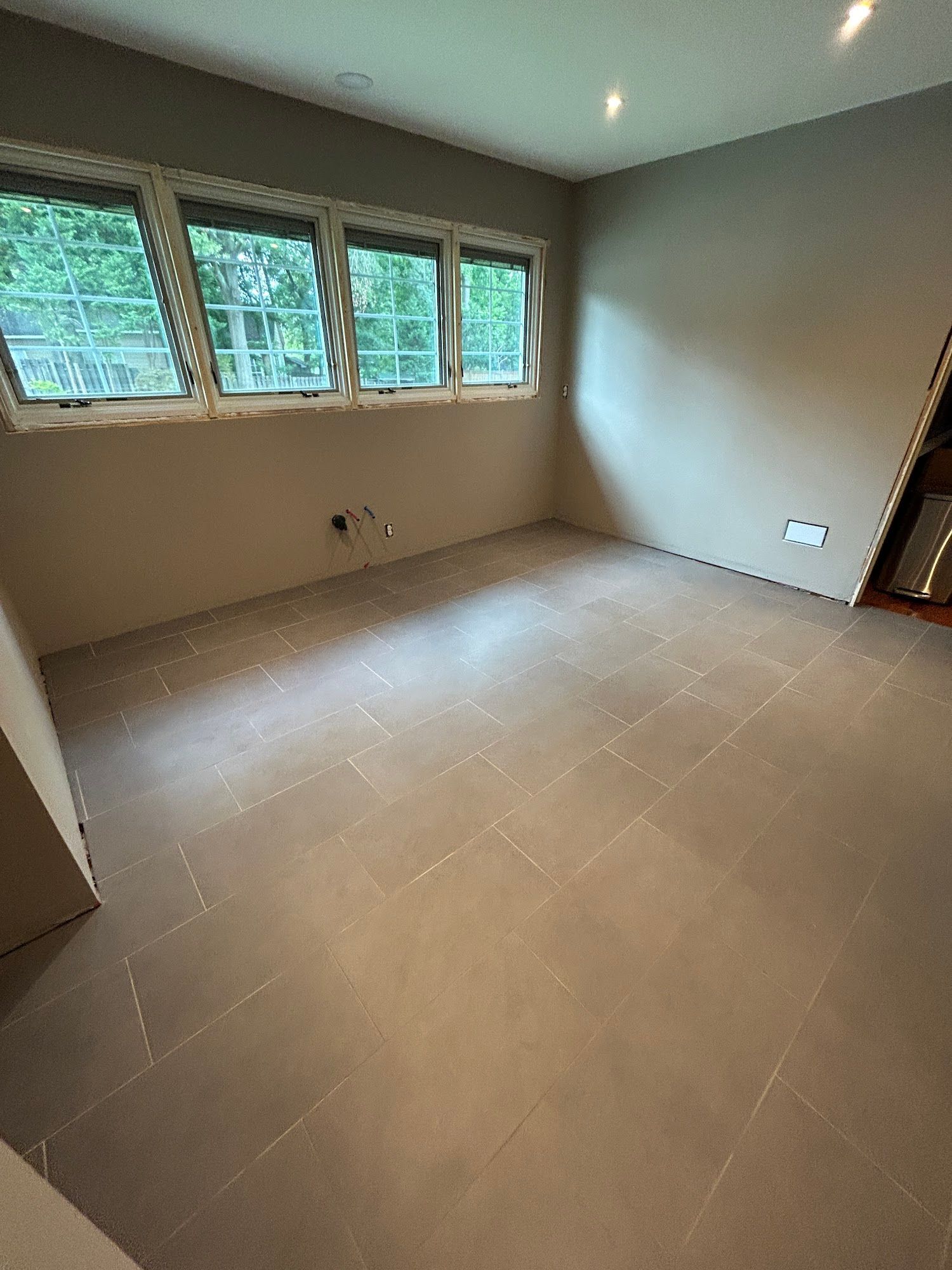 Empty room with light gray tile floor and walls, windows on the left side, and a door on the right.