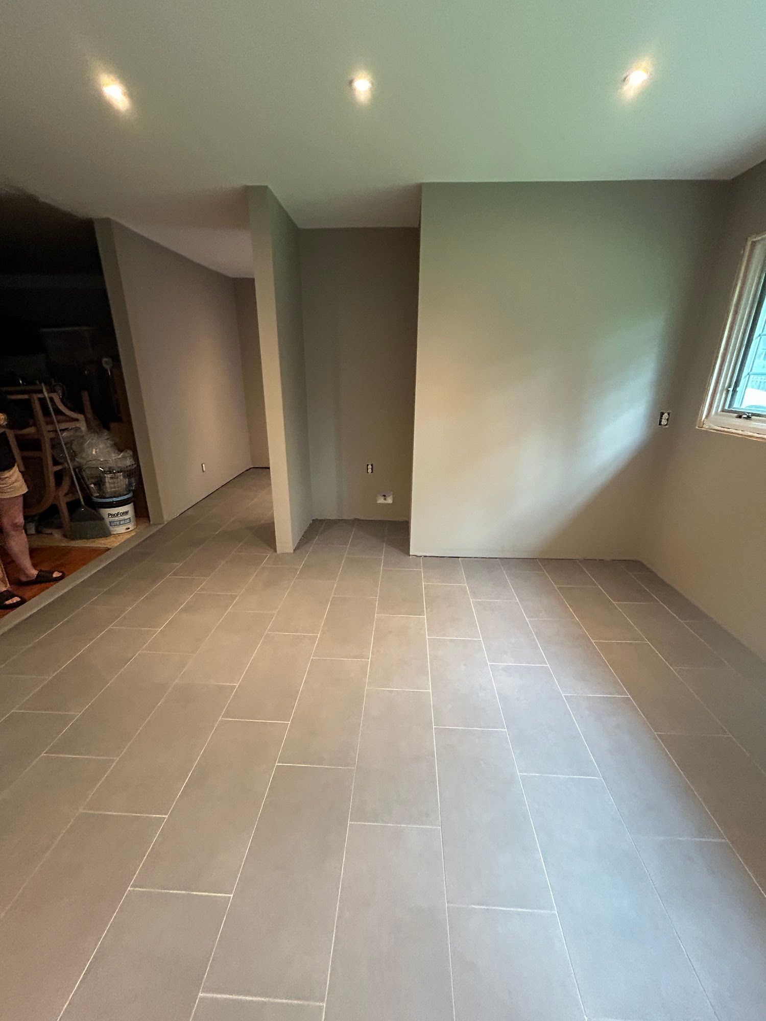 Newly tiled room, gray walls, recessed lighting, small window, partially constructed.