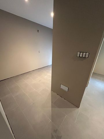 Empty room with beige walls and gray tiled floor. A light switch panel is visible.
