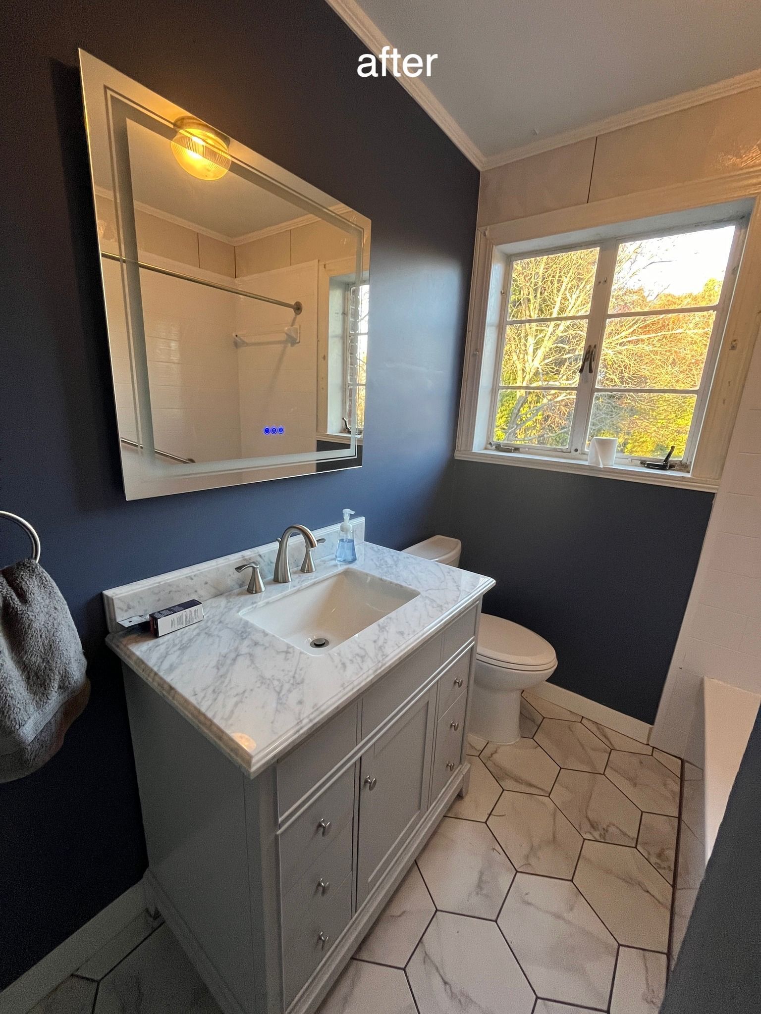 Bathroom with navy blue walls, marble vanity, hexagon tile floor, large mirror, and window.