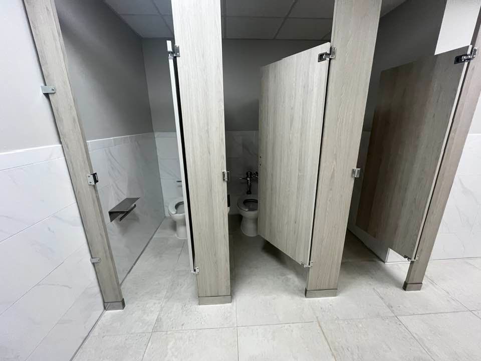 Public restroom with light-colored stalls, gray walls, and white tile floor.