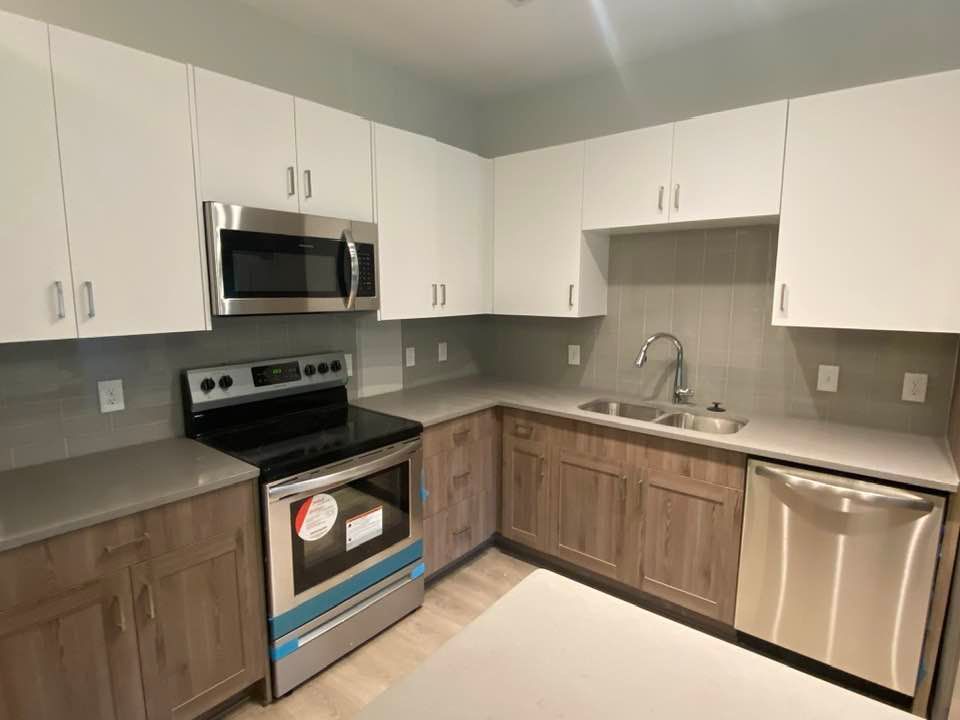 Modern kitchen with white and wood cabinets, stainless steel appliances, and gray countertops.
