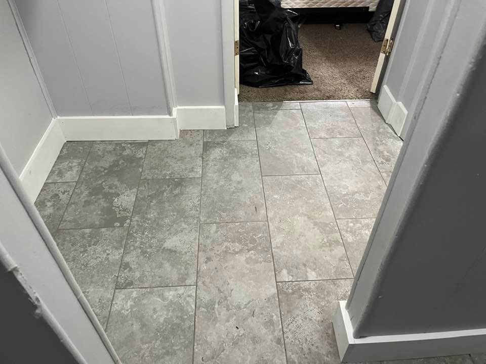 Gray tile hallway leading to a room with a black trash bag.