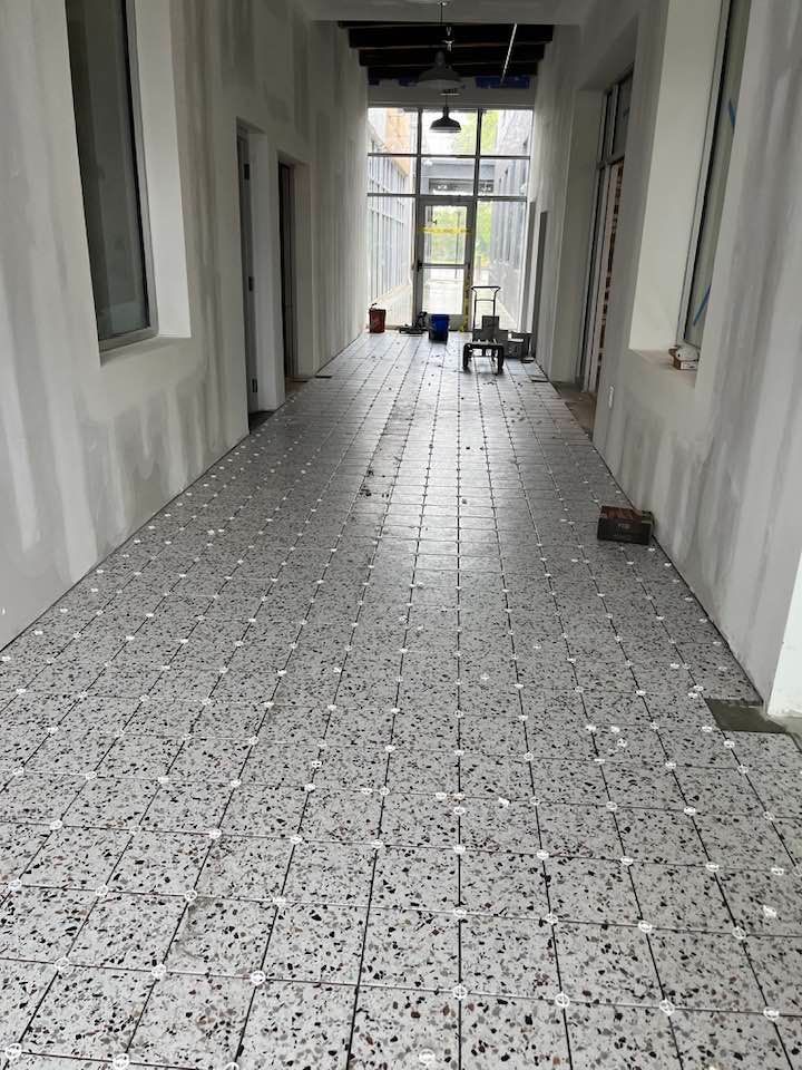 Hallway with newly laid speckled tiles; unfinished walls, windows at the end, construction materials present.