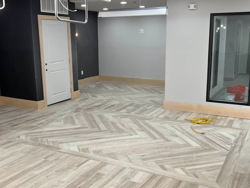 Room with light wood-look herringbone tiled floor, white door, and gray and black walls.