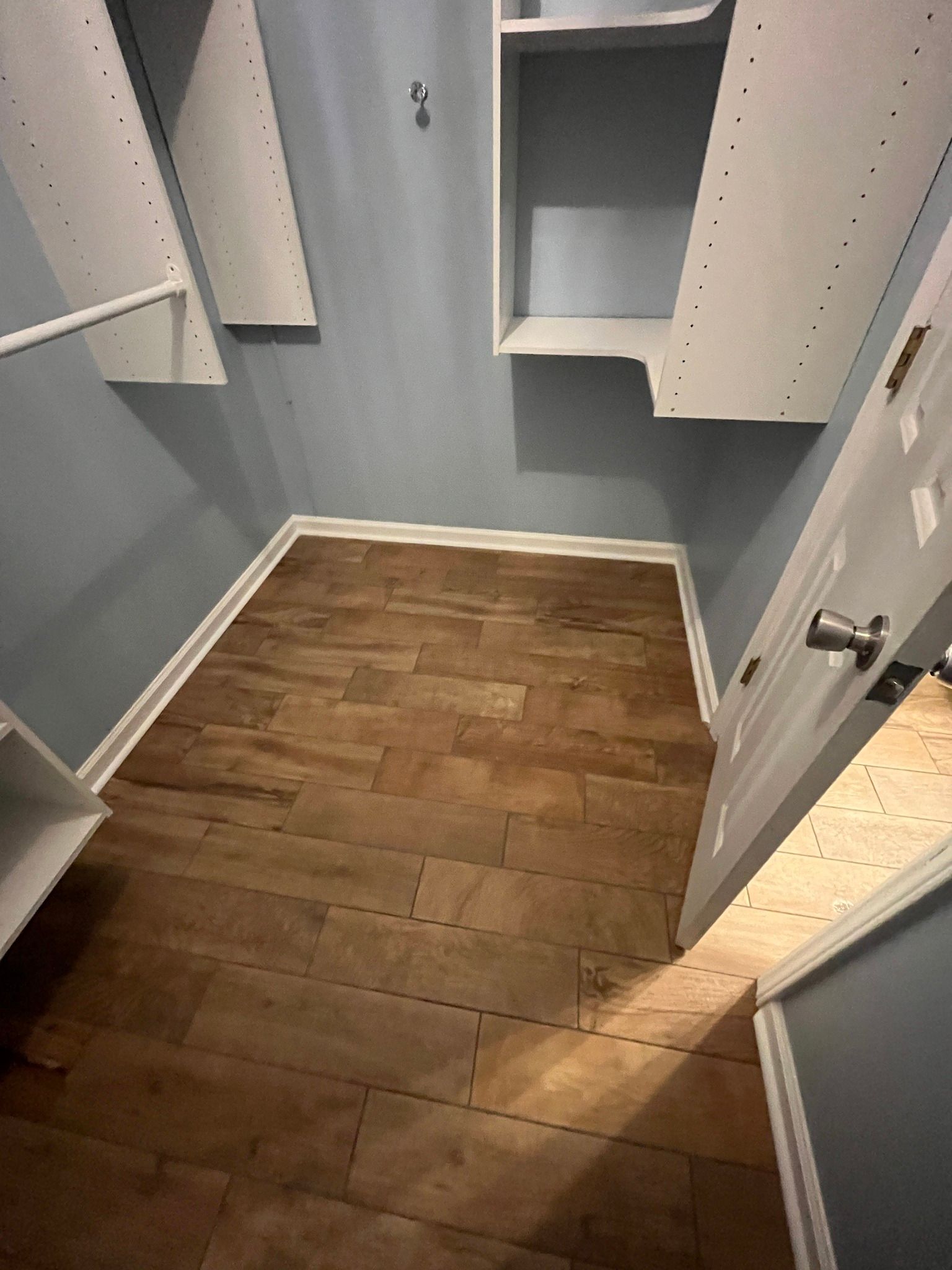 Closet interior with wood-look flooring, light blue walls, white shelves and door, and a silver handle.