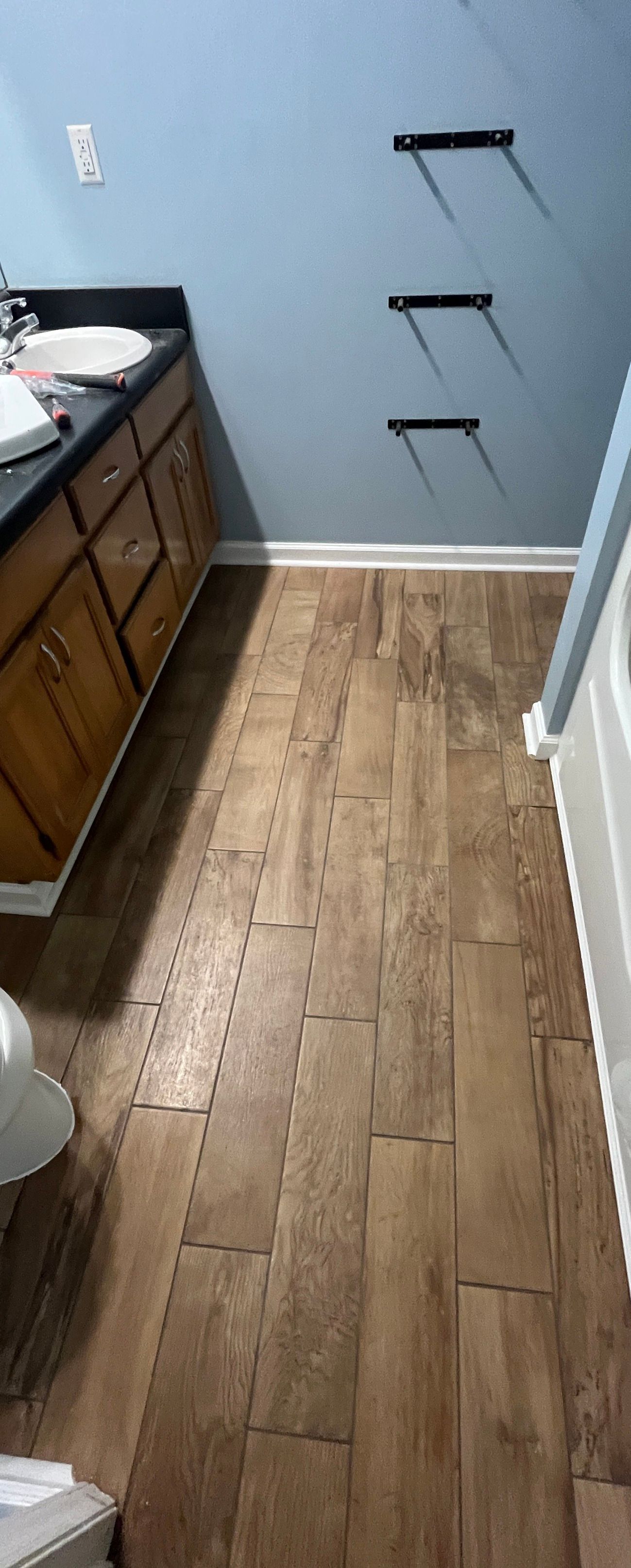 Bathroom interior with wood-look floor, blue walls, wooden cabinets, and three black shelf brackets.