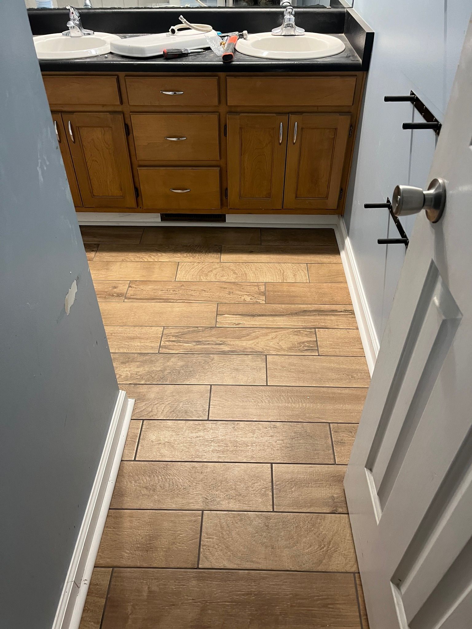 Bathroom with wooden floor, wooden vanity, and two sinks. A partially opened white door on the right.