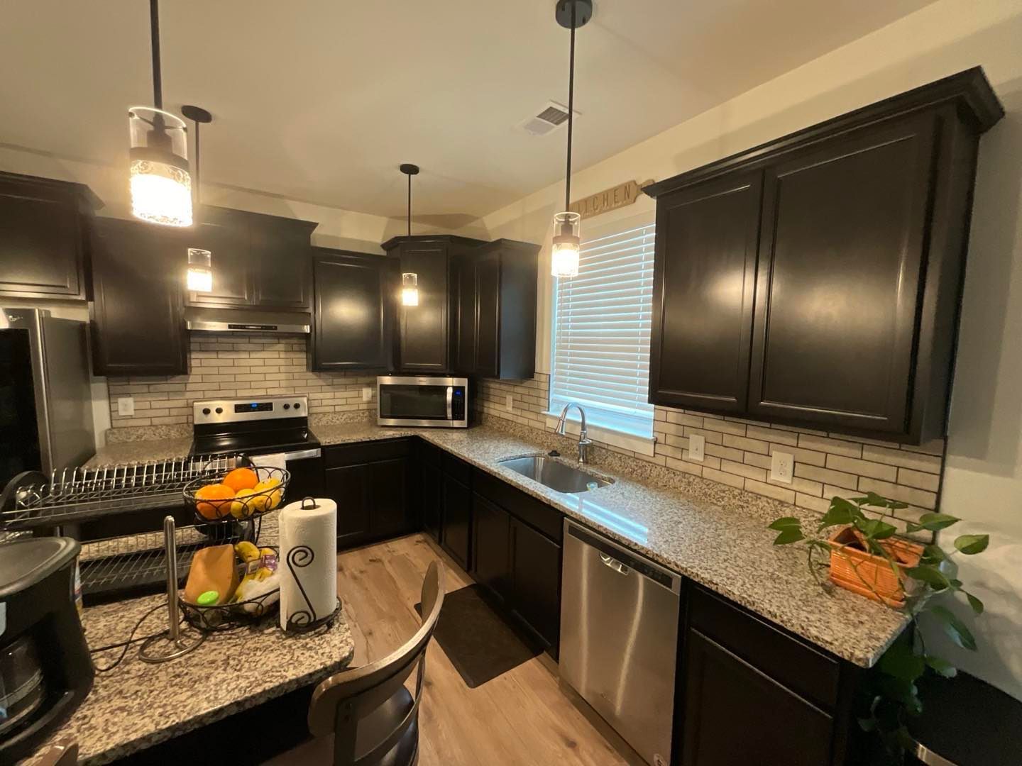 Dark kitchen with granite countertops, stainless steel appliances, and overhead lighting.