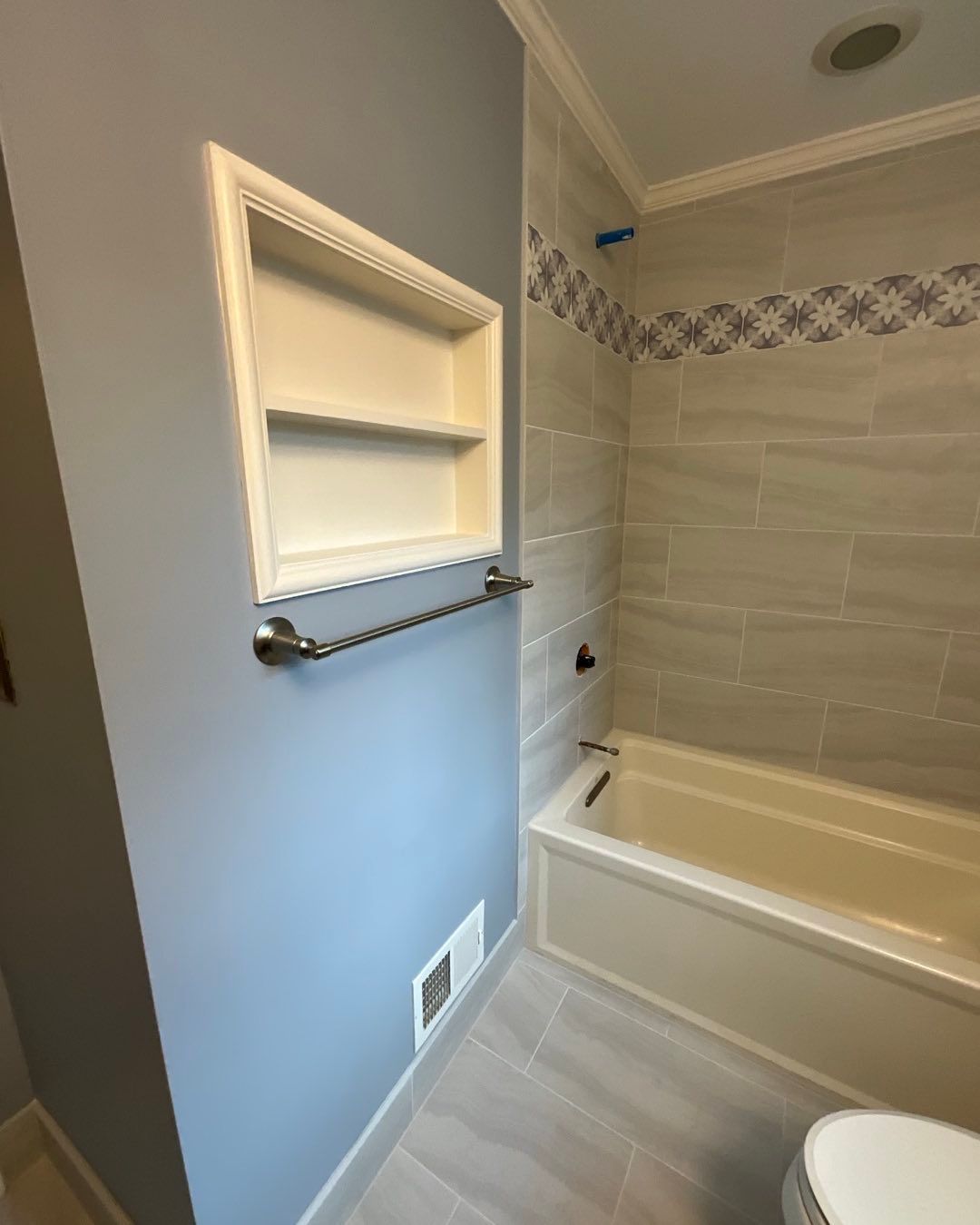 Bathroom interior with recessed shelf, towel bar, bathtub, and blue walls.