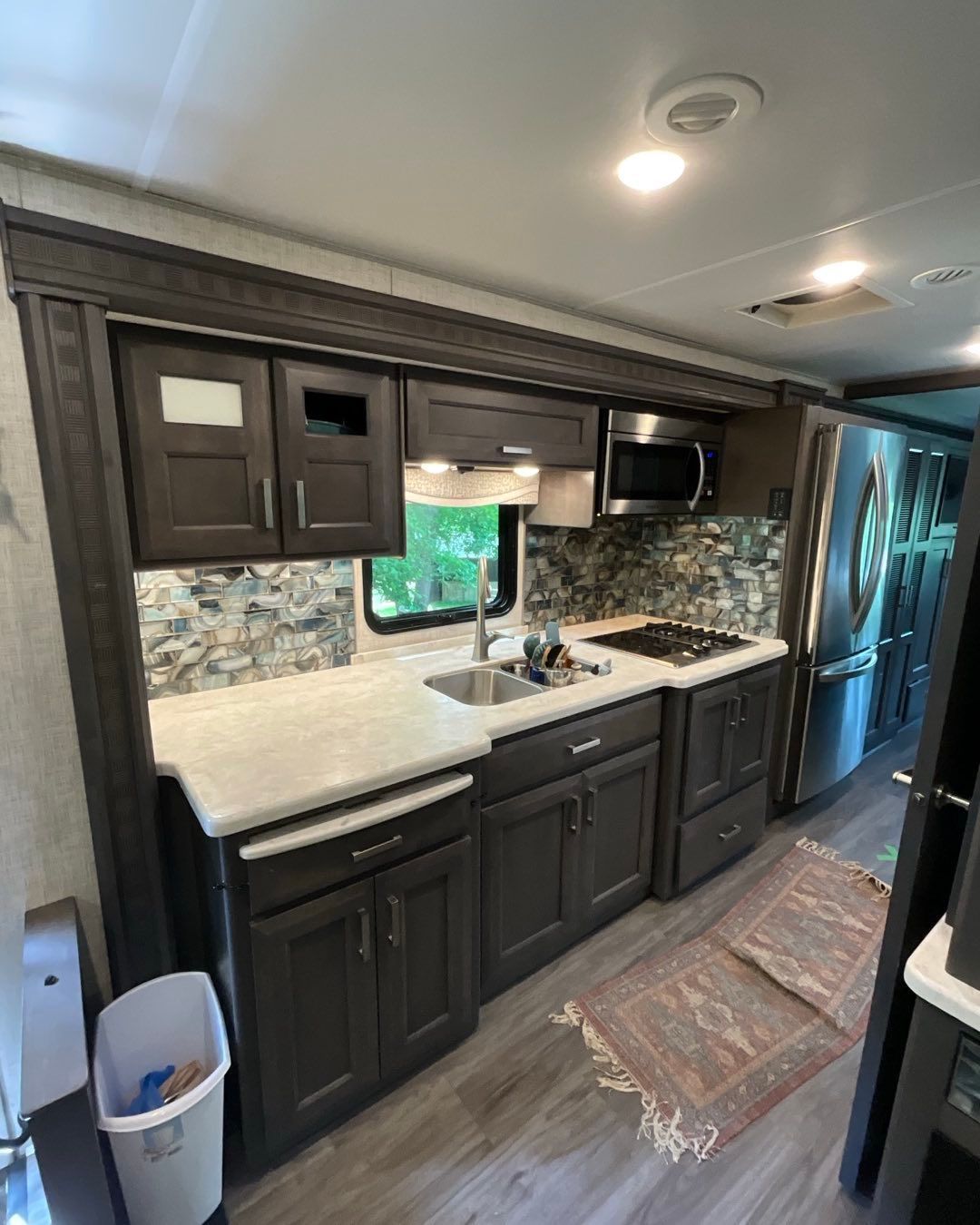 RV kitchen with dark cabinets, stainless steel appliances, and a mosaic backsplash.