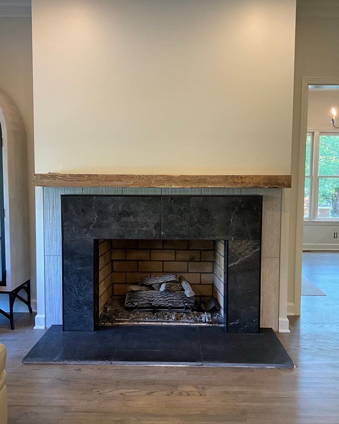 Fireplace with black stone surround, brick interior, and wood mantel, in a room with hardwood floors.