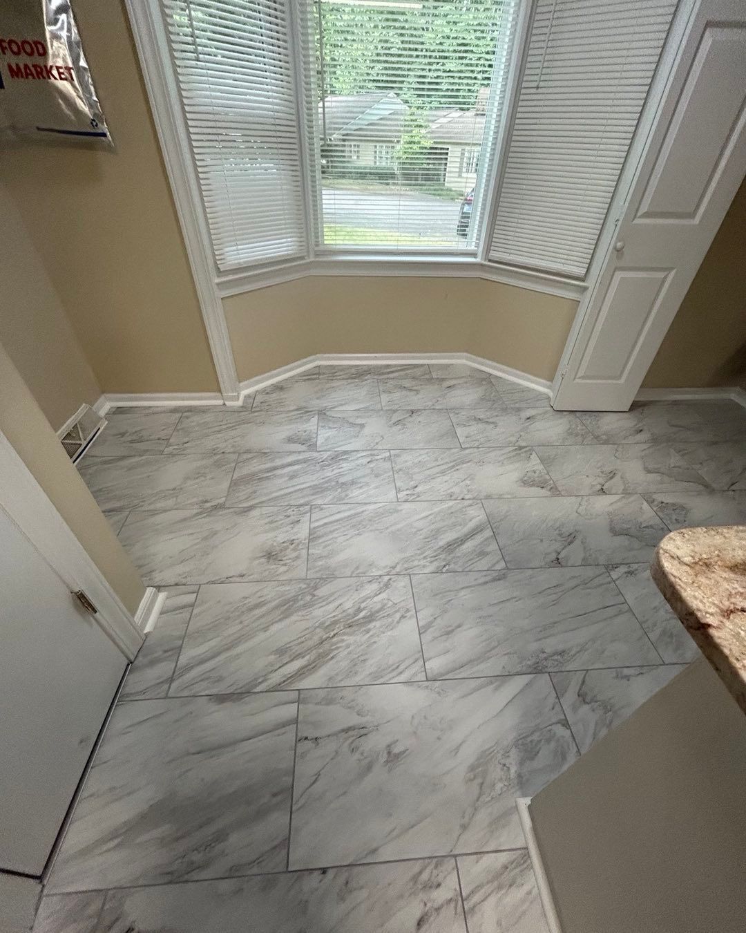 Tiled floor with marble-like pattern by a bay window with white shutters, light walls and trim.