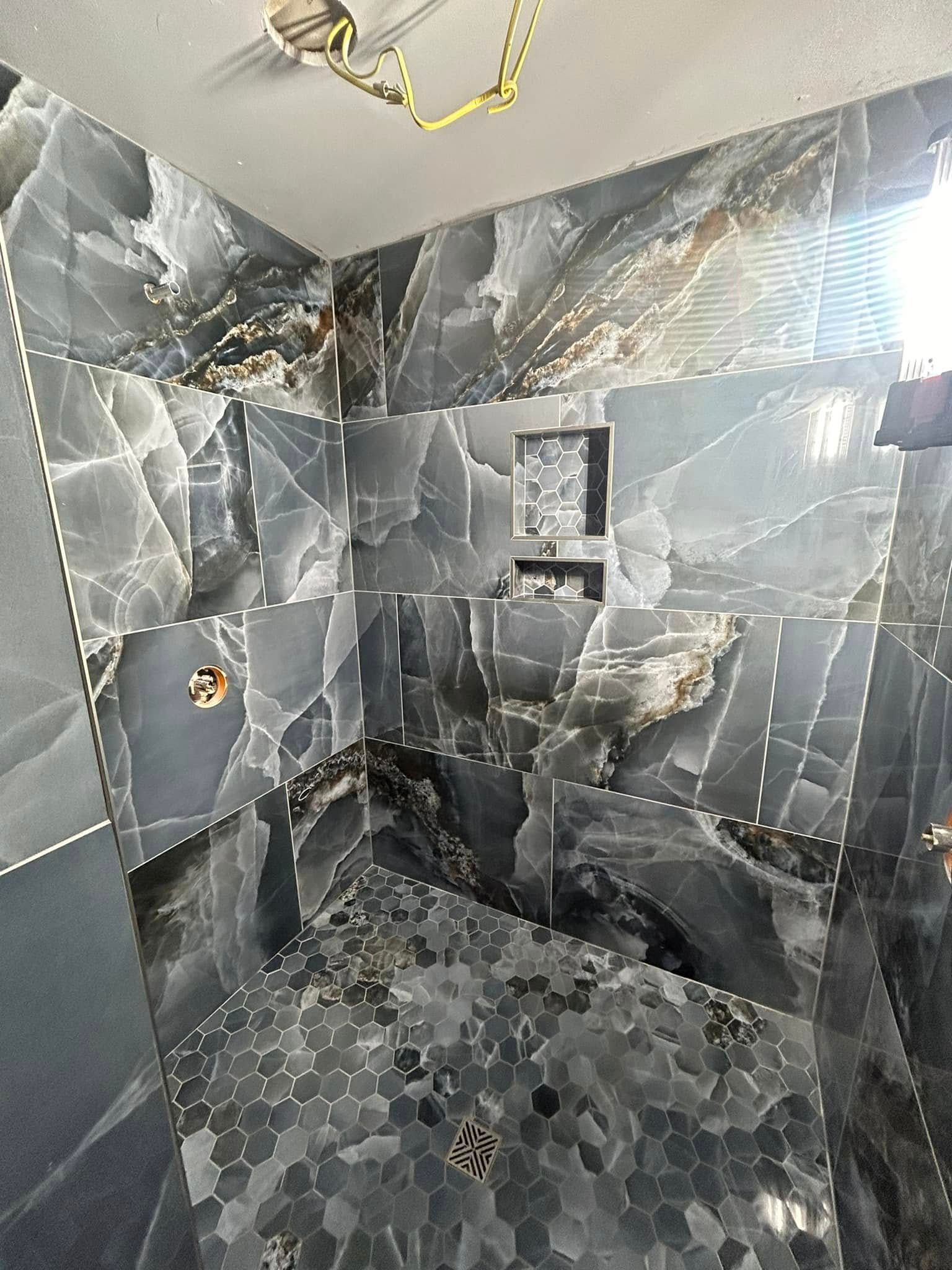 Dark gray and black tile shower with a recessed shelf and gold fixtures.