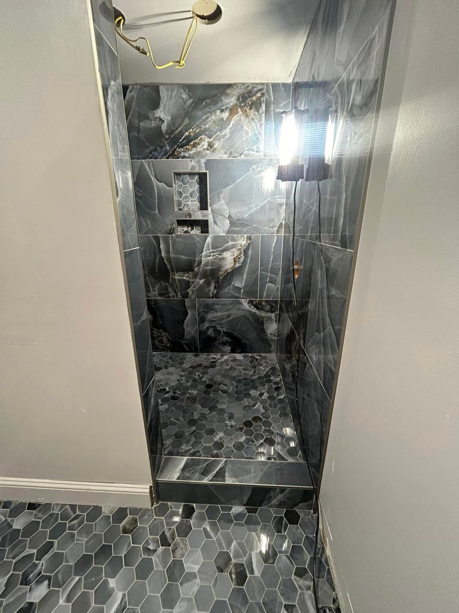 Dark tiled shower with a niche, hexagon-tiled floor, and a rectangular opening.