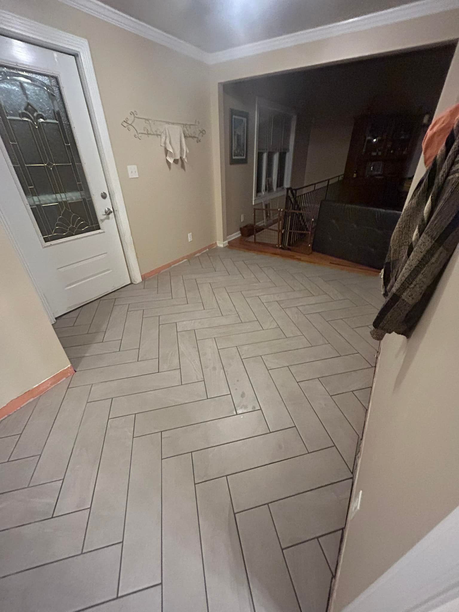 Herringbone-patterned floor in a home entryway, with a white door and neutral-colored walls.