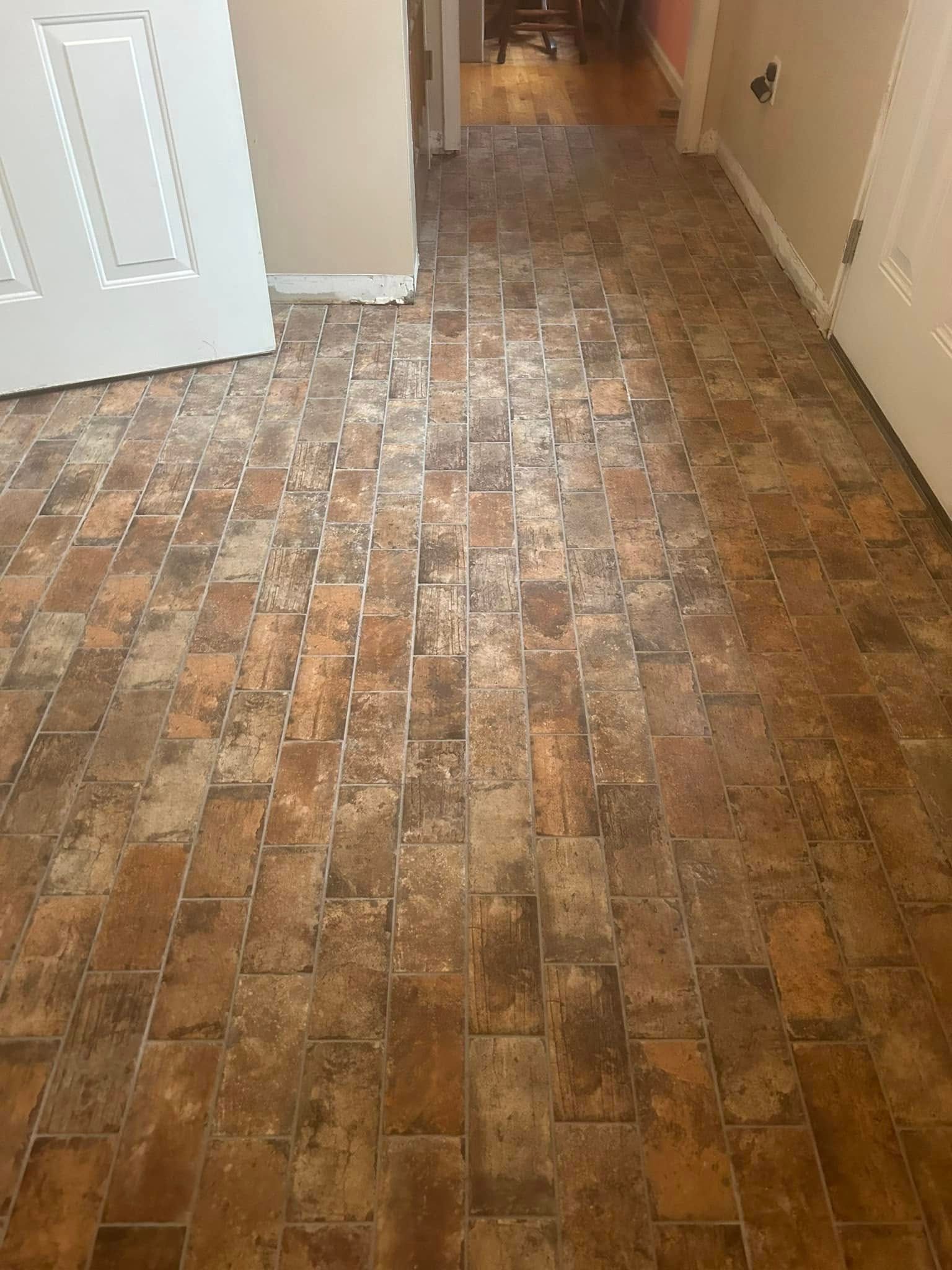 Brown and tan tile flooring in a hallway, with white doors and beige walls.