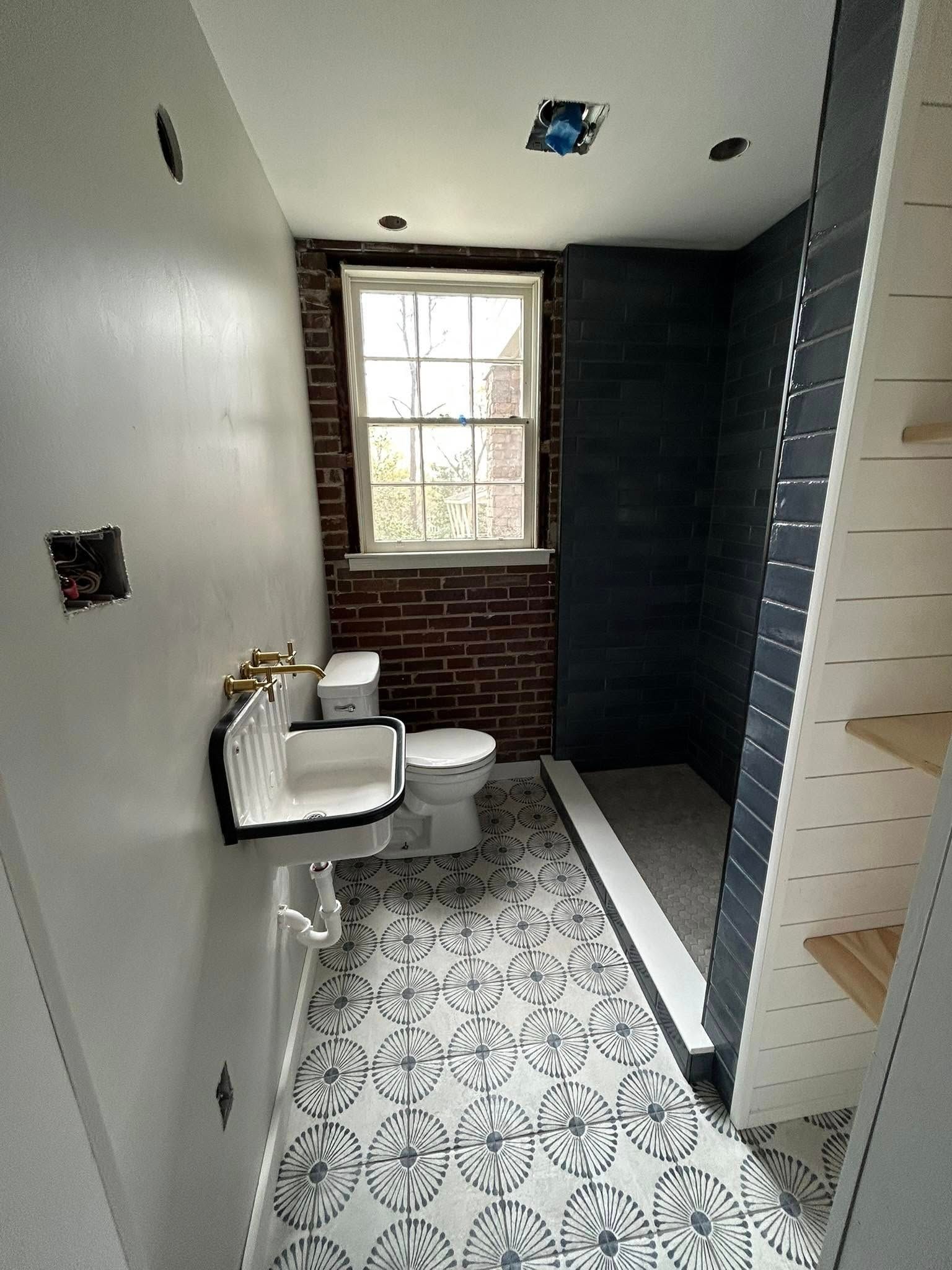 Bathroom under construction with brick wall, patterned tile floor, and sink.