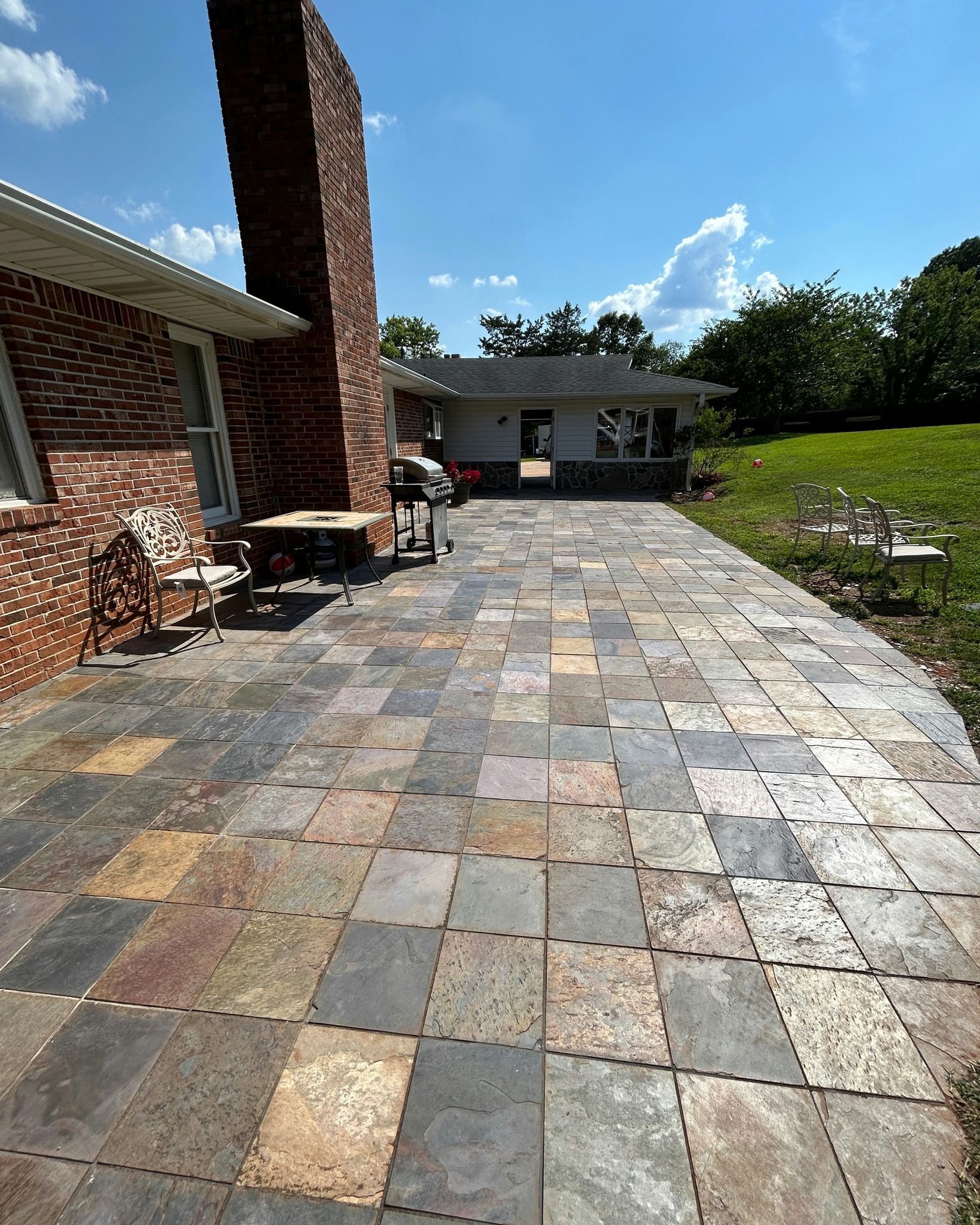 Brick patio with multiple colors, extending from a brick building with a chimney. Sunny day.