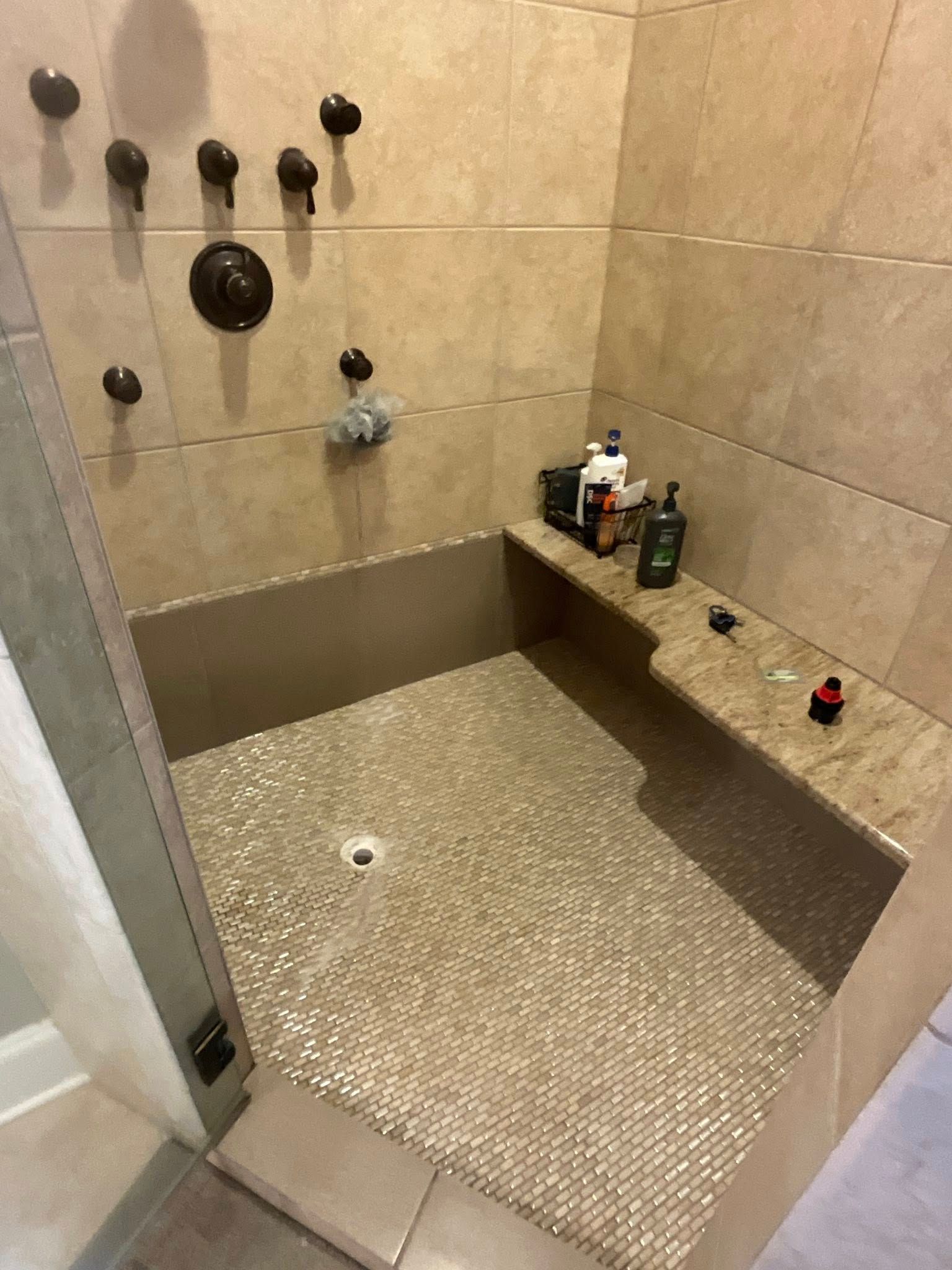 Tiled shower stall with built-in bench, bronze fixtures, and pebble tile floor.