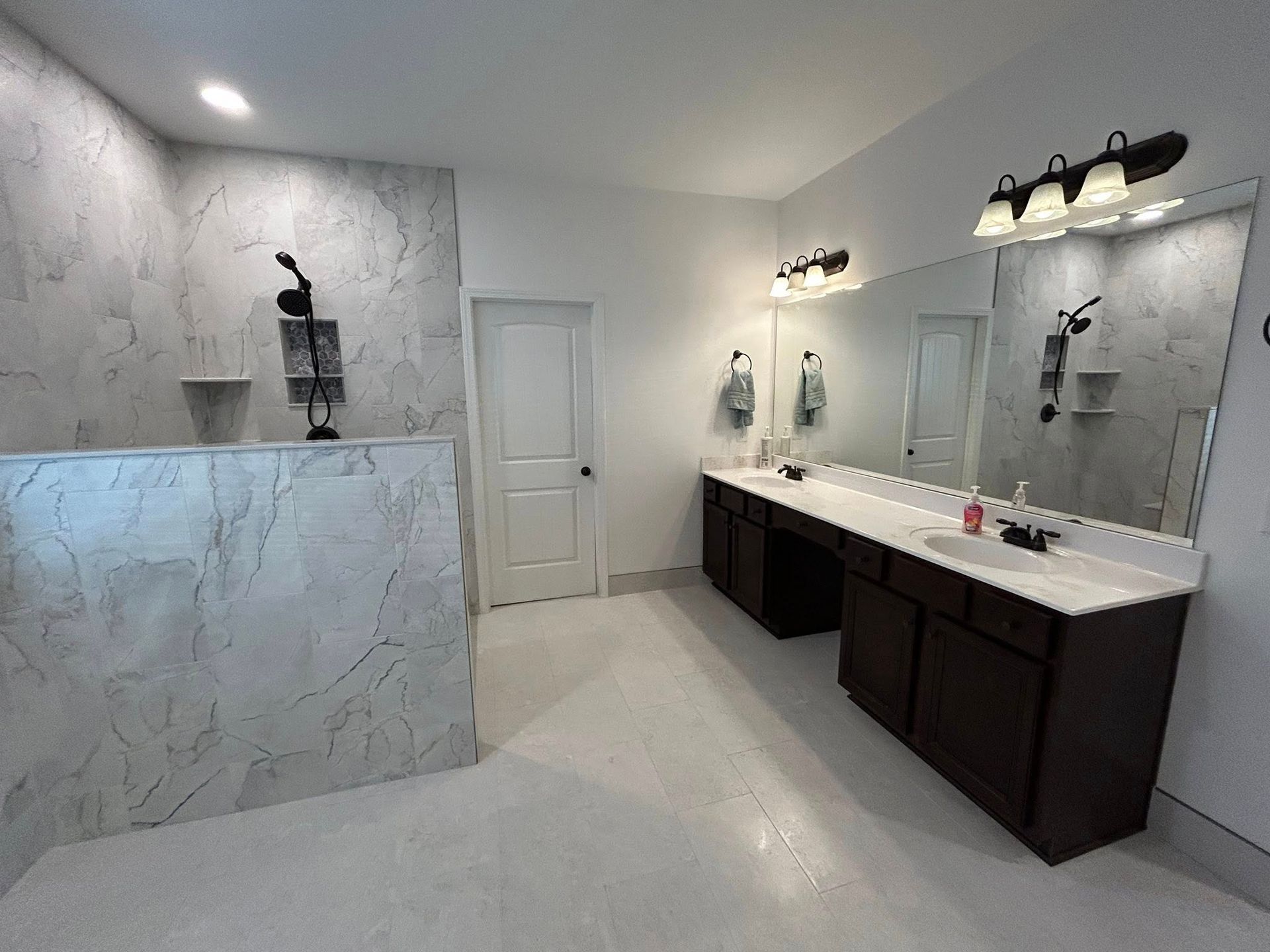 Spacious, bright bathroom with marble-look shower, double vanity with dark cabinets, and white floors.