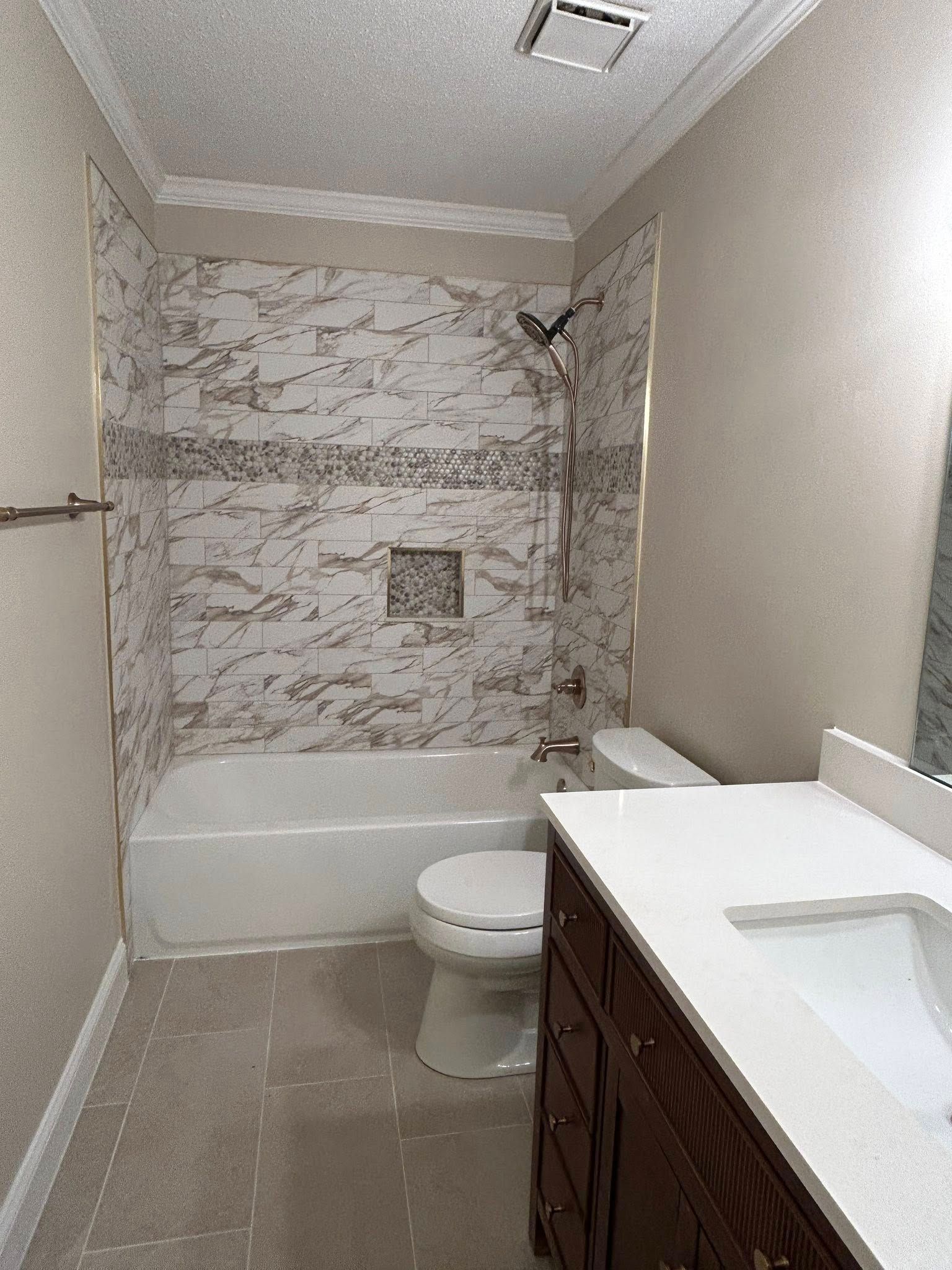 Bathroom with white tub, toilet, vanity, and marble tile walls.