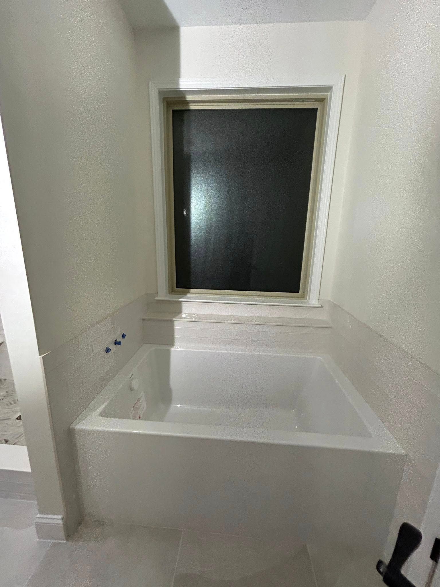 A bathtub next to a window in a bathroom with walls covered in a textured, light material.