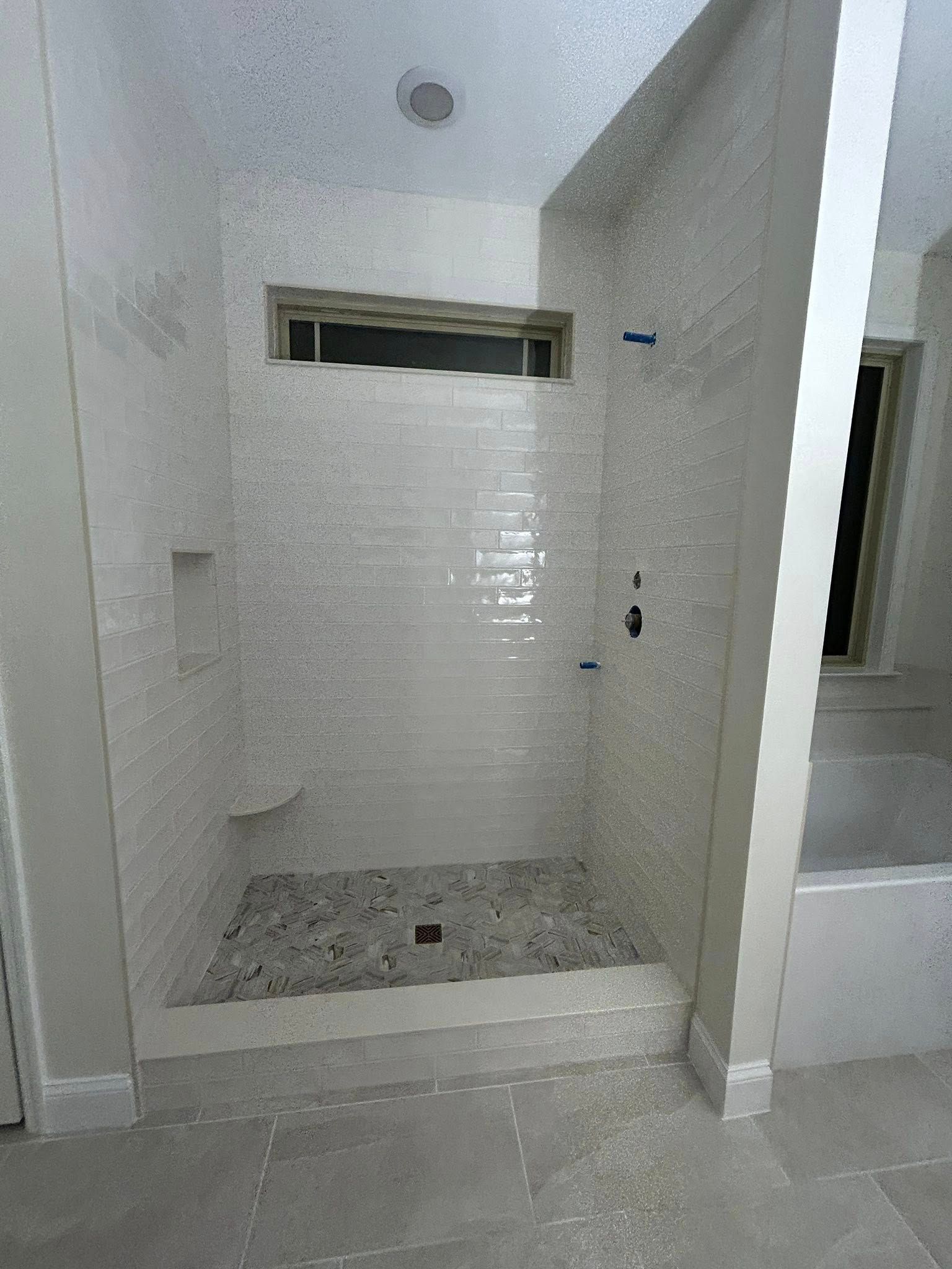 White tiled shower with pebble floor, built-in shelf, and black shower fixtures.