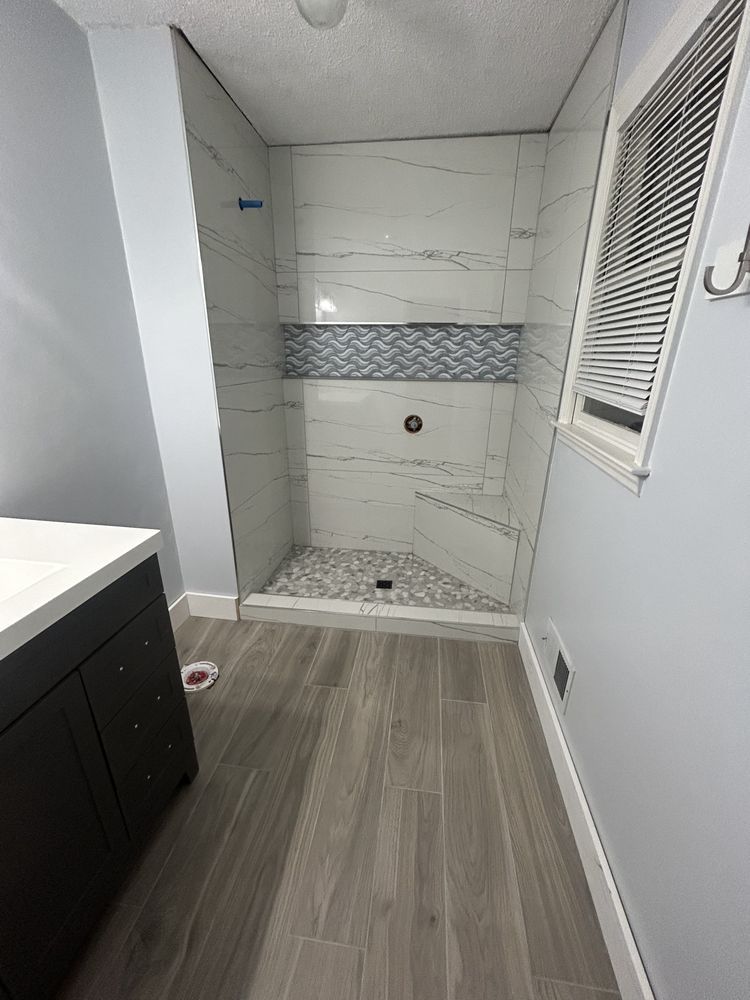 Newly tiled shower with gray and white tile, a dark wood vanity, and a window.
